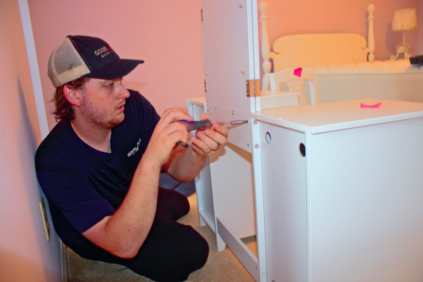 A man assembling white furniture using a screwdriver indoors.